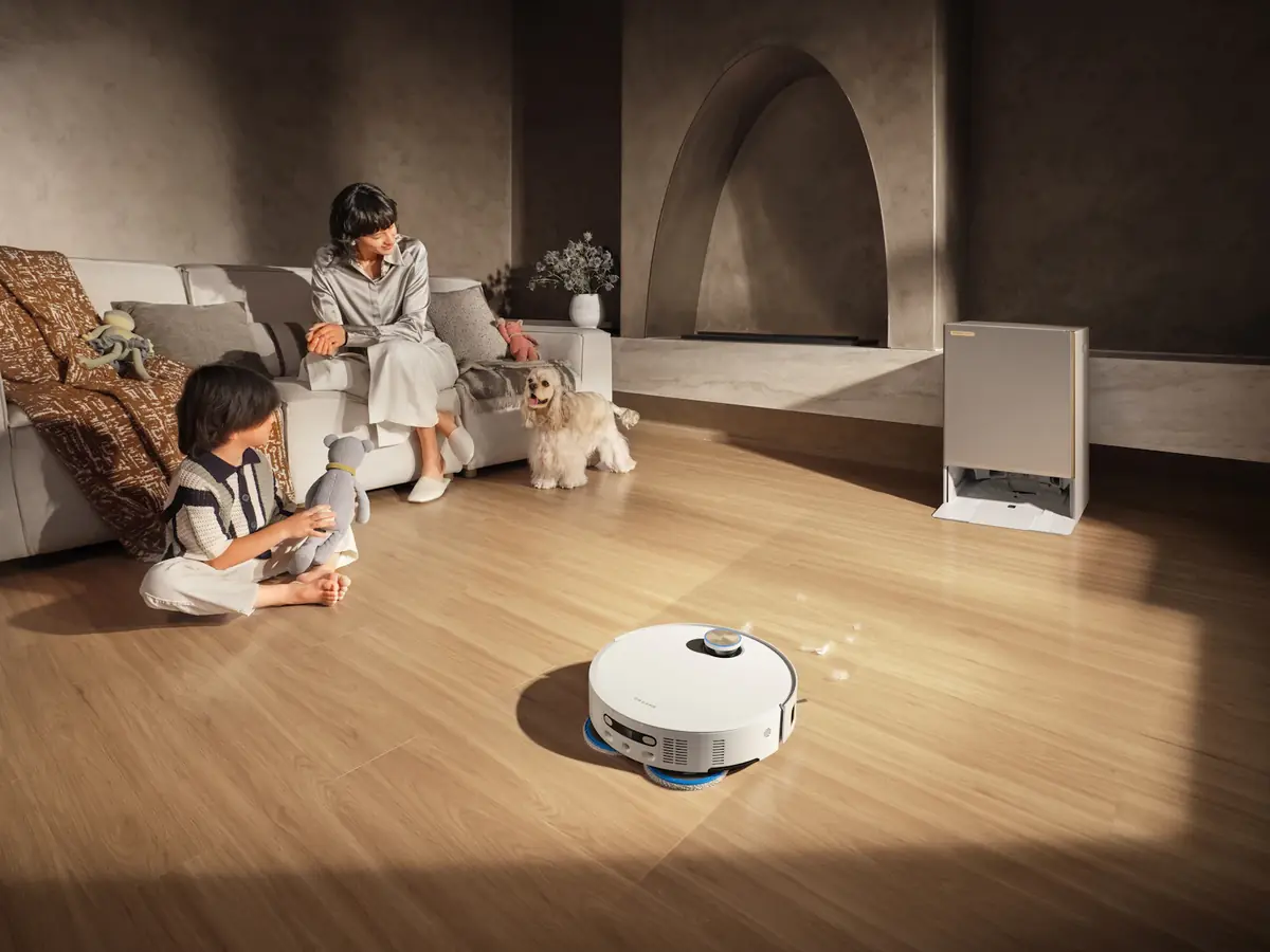 Un robot aspirateur autonome nettoie le parquet d'un salon pendant qu'une famille joue avec son chien
